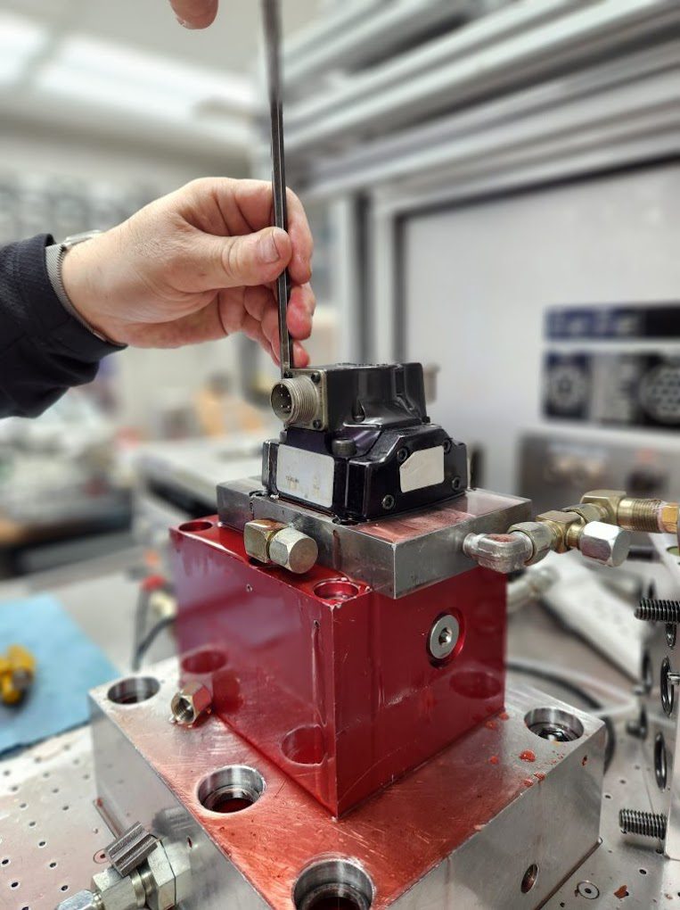 A technician interfacing with a modern servo valve with digital controls at an NC Servo Technology testing station.